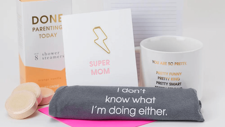 Components of a mother's day product bundle, which include a towel, shower steamers, a notepad, a mug, and a card that says s