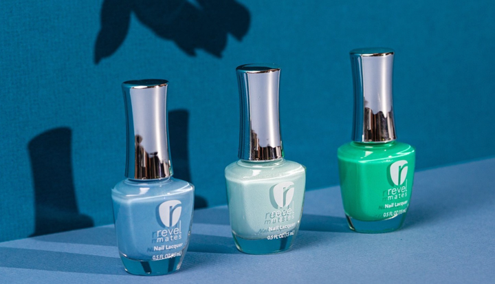 Three bottles of Revel Nail nail polish in blue, mint, and green. The background behind them in blue and they're placed in a